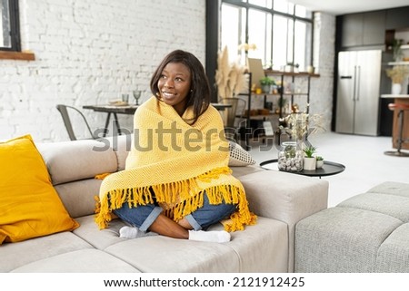 Good morning. Young multiracial teenage girl covered in a cozy yellow soft blanket staying at home at the warm sofa, looking in the window, feeling happy and blessed Royalty-Free Stock Photo #2121912425