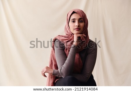 Portrait of confident young Middle Eastern woman wearing hajib looking at camera with hand on chin Royalty-Free Stock Photo #2121914084