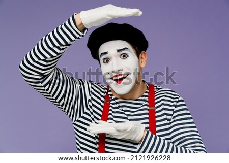 Charismatic crazy amusing amazing young mime man with white face mask wears striped shirt beret making hands photo frame box gesture isolated on plain pastel light violet background studio portrait Royalty-Free Stock Photo #2121926228