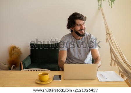 Young business man working at home in his kitchen with laptop and papers on kitchen wooden desk. Gray notebook for working. Home office concept. High quality photo