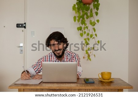 Young business man working at home with laptop on a brown arm chair. Gray notebook for working. Home office concept. High quality photo