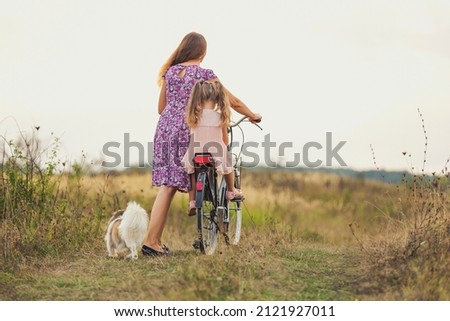 mother and daughter walking with a bicycle and a dog in nature