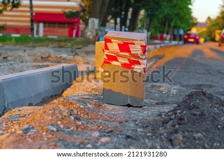 Concrete block wrapped with striped tape stands on the road as a warning sign about the work.