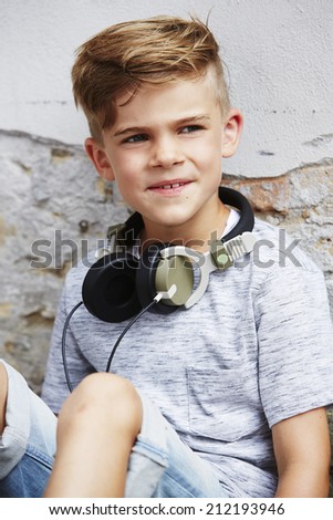 Boy wearing headphones and sitting against wall 