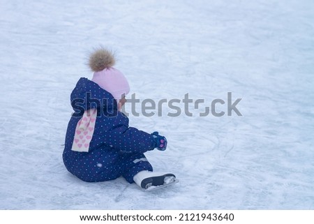 Baby girl caucasian learns to skate at the ice rink in winter falls and laughs.