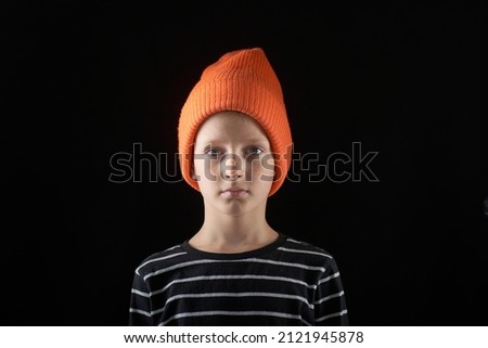 Portrait of a boy 10 years old in an orange cap on a dark background