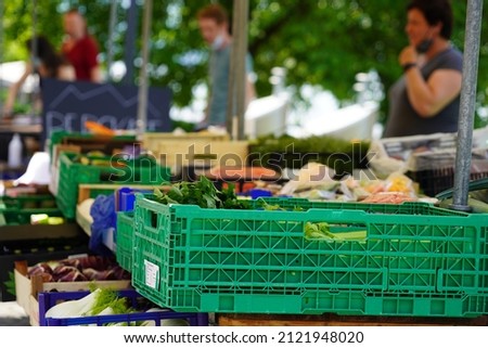 Market stall with vegetables and fruits. There are defocused persons on the background. The different types of vegetables are in green plastic crates. 