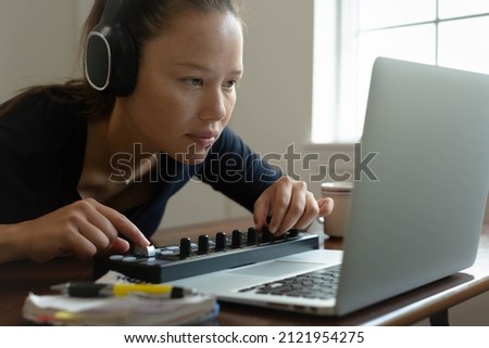 A woman wearing headphones and using her computer at home. Making music and editing photos.