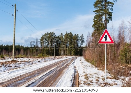 Melting ice on a country road in winter day. Road junction with priority over minor road from the left
