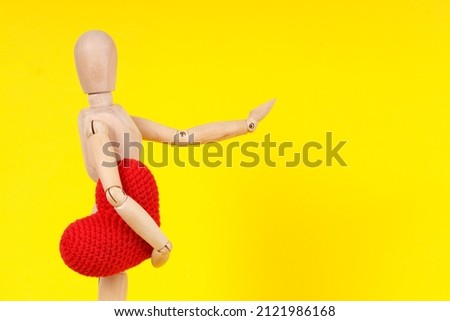 wooden man with a red heart in his hands on a yellow background. High quality photo