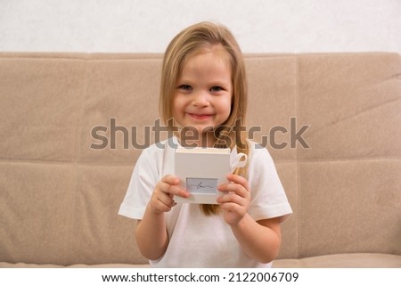 A little blonde girl is sitting smiling and holding a white box in her hands with the inscription Love. Gift concept