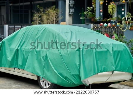 A car covered in green tarpaulin, to protect it from the weather.              Royalty-Free Stock Photo #2122030757