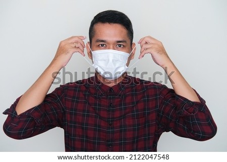 Closeup portrait of adult Asian man going to wear medical mask with serious expression  Royalty-Free Stock Photo #2122047548