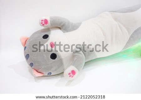 Toy plush cat with stripes on the head and a white belly, red paws - light background with green illumination