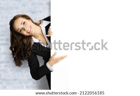 Happy excited smiling woman in black confident suit showing white banner signboard. Business and advertising concept. Copy space area. White bricks loft wall background.