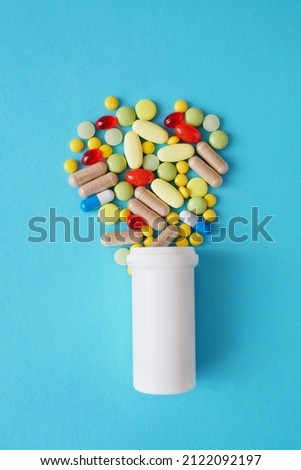 drugs, pills and capsules and white bottle on blue background, closeup