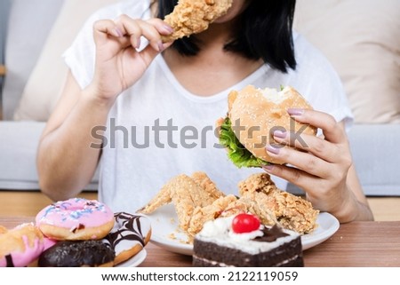 Binge eating disorder concept with woman eating fast food burger, fired chicken , donuts and desserts  Royalty-Free Stock Photo #2122119059