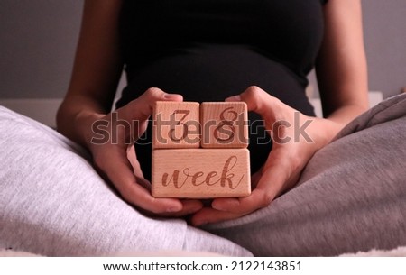 Pregnant woman holding cubes of 38 weeks of pregnancy against the background of her belly