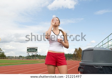 Young woman drinking water out of a water bottle at a track. Horizontally framed photo