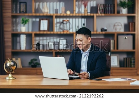 Successful and happy businessman, shopping online in an online store, Asian man working in a modern office, using a laptop, holding a credit card