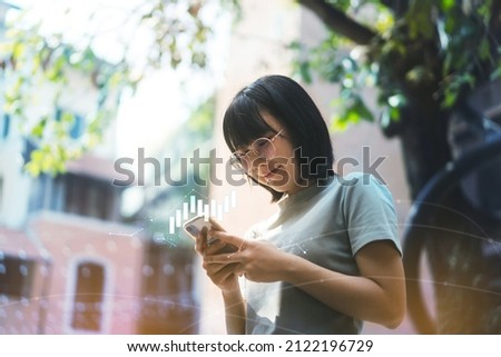 Young adult happy asian woman wear eyeglasses using mobile phone trade crypto cion and nft for money profit with digital graph. Poeple investment trend in metaverse concept. Royalty-Free Stock Photo #2122196729