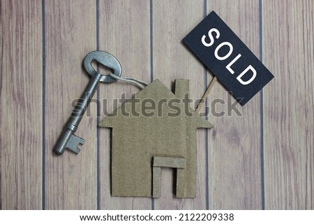 Sold text on dark paper with house model and key on wooden desk. Property investment concept.