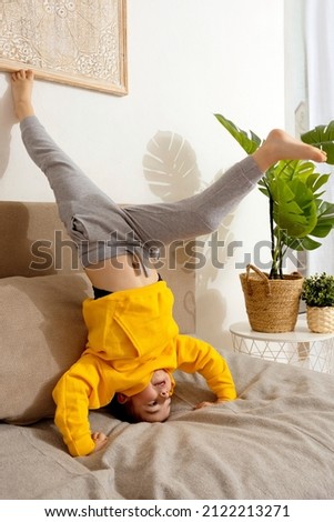 Little caucasian boy doing gymnastic handstand exercise in living room. Child standing on hands upside down and having fun. Sport at home. Workout in the apartment. Healthy lifestyle.