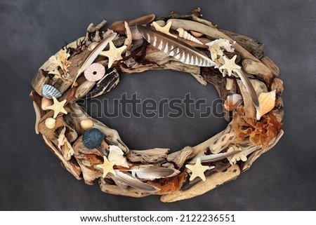 Treasure of the sea abstract driftwood, seashell, feather and seaweed oval shaped wreath on grunge grey background. Natural element with copy space. Top view, flat lay.
