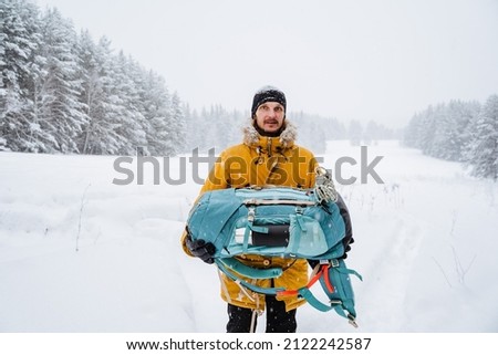 happy traveler carries a backpack in his hands. Bright hiking backpack with equipment,Snowy forest and rocks. Climbing the mountain in winter. Survival in the wild. High quality photo