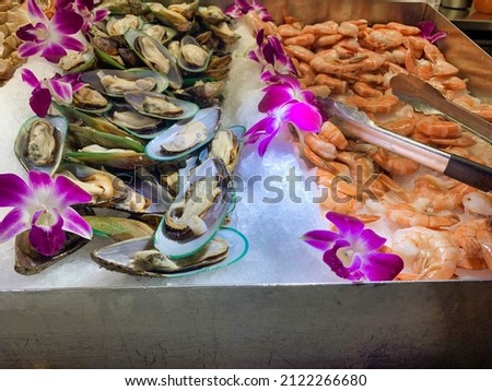 View of fresh uncooked shrimp and open oyster shells on top of ice at a buffet restaurant.