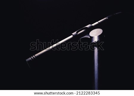 Closeup view of studio microphone on stand in dark, highlighted shapes. 