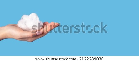 Banner with hand holding cotton cloud at blue sky background. Dreaming or cloudy weather concept in surrealism style. Place for text. High quality photo Royalty-Free Stock Photo #2122289030