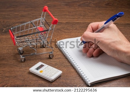 Man calculates the budget. Shopping cart a on table with calculator and paper. Budget of poor and low income family. Rising food and grocery store prices and expensive daily consumer goods concept Royalty-Free Stock Photo #2122295636