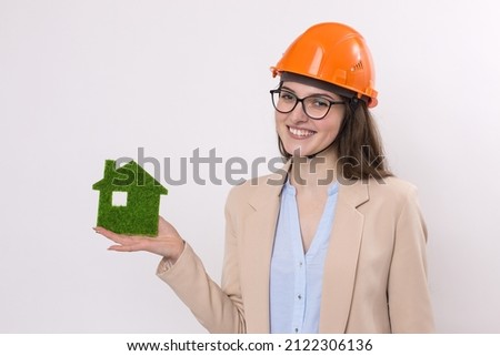 A girl in a construction helmet holds a green house. The concept of ecological clean housing.