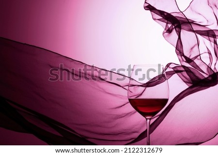 Glass of red wine on a background of waving satin curtain. Copy space.