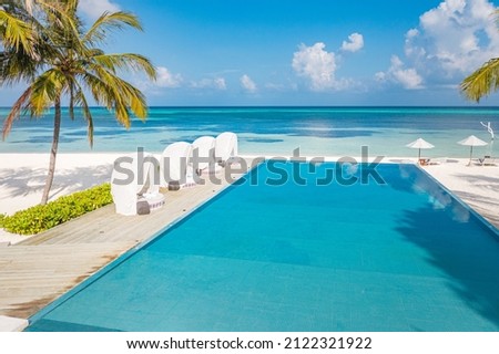 Outdoor tourism landscape. Luxurious beach resort with swimming pool and beach chairs or loungers under umbrellas with palm trees and blue sky. Exotic summer travel and vacation background concept Royalty-Free Stock Photo #2122321922