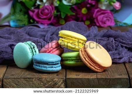 French macaroni on the background of a beautiful bouquet of flowers lie on a wooden background. Close-up. 