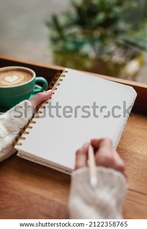 Unidentified woman is writing in the notepad in cafe. Working on bullet journal, diary, morning pages, plans and goals. Soft focus Royalty-Free Stock Photo #2122358765