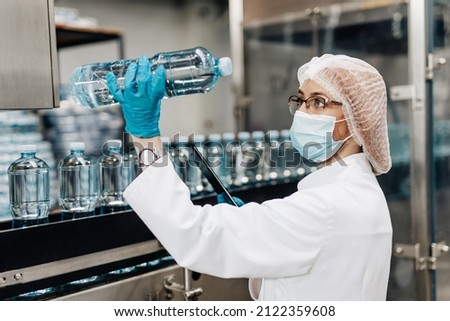 Beautiful female worker in workwear and with protective mask on her face working in bottling factory. Inspection quality control.  Royalty-Free Stock Photo #2122359608