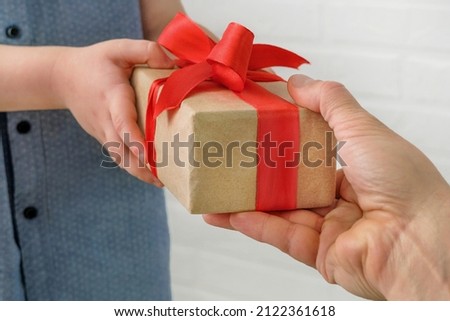 a gift with a red ribbon in male and children's hands. Close-up. A father gives a gift to his son, or a son gives a gift to dad on Father's Day. horizontal photo