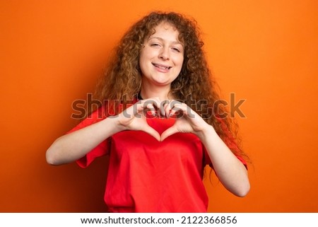 Picture of a smiling woman in soccer football uniform red color showing heart sign using two hands, football support concept.