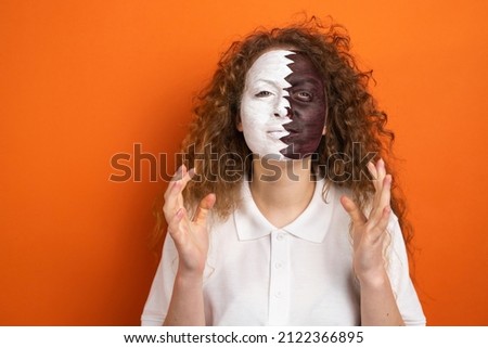 Close up picture of a qatar fan football woman with red hair and face painted in national flag of qatar football team.
