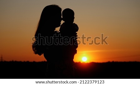 Caring mother holds the baby in her arms and kisses him, unrecognizable silhouette at sunset, motherly love Royalty-Free Stock Photo #2122379123