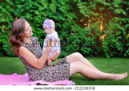 Mum holds on hands of a little daughter outdoors in park