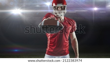Portrait of confident male american football player offering ball at illuminated sports field. competitive sport and challenge.