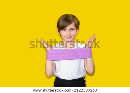 the schoolboy does exercises with an elastic band for sports or an expander. happy child athlete, the boy is training. yellow background