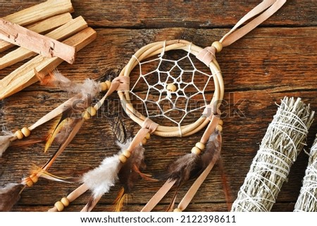 A close up image of a dreamcatcher with healing smudge sticks on a wooden table top. 