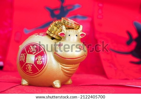 Gold bull piggy bank on a festive red background carrying a pile of gold coins.The Chinese characters in the picture mean: "to attract wealth and treasure"