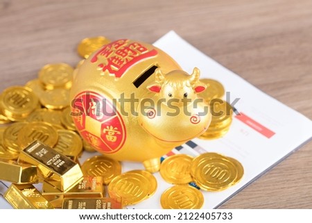 The Taurus piggy bank is surrounded by a pile of gold bars and coins on the file.The Chinese characters in the picture mean: "to attract wealth and treasure"