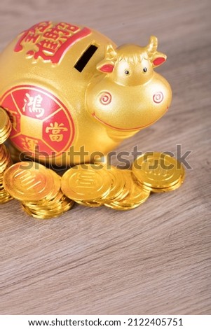 The Taurus piggy bank is surrounded by a pile of gold bars and coins on the file.The Chinese characters in the picture mean: "to attract wealth and treasure"